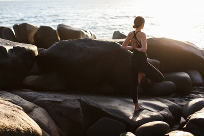 白天，一个身穿黑色比基尼的女人站在海边的岩石上